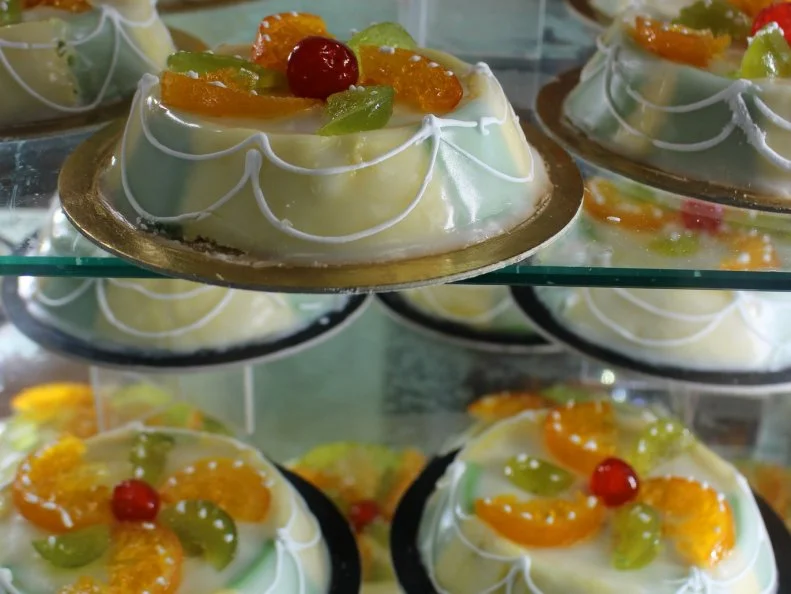 View of a display of Cassata siciliana, a traditional dessert from Sicily, Italy. Cassata consists of round sponge cake moistened with fruit juices or liqueur and layered with ricotta cheese and chocolate chips. It is covered with a shell of marzipan, pink and green pastel colored icing, and decorative designs. The cassata is topped with candied fruit depicting cherries and slices of citrus fruit characteristic of Sicily.