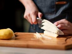 Woman cutting potato in a domestic kitchen at home wearing apron above the cutting board. Homemade food abstract.