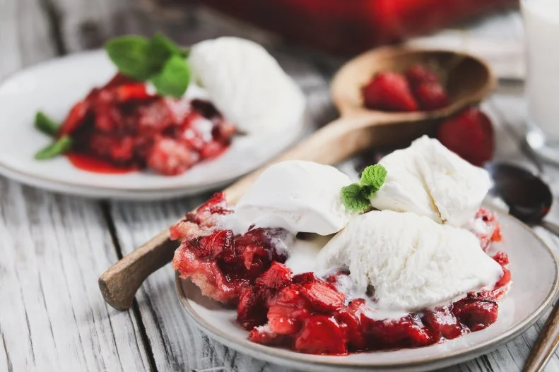 Sweet homemade strawberry cobbler or Sonker with French vanilla ice cream over a rustic white wood table. Extreme selective focus with blurred background.