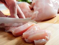 Man's hand cutting raw chicken breast. Selective focus