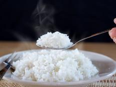 Asian woman hand eating cooked hot rice by spoon in a white plate