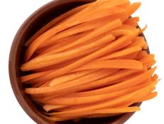 Raw Carrots cut into chopsticks in a bowl isolated on a white background, top view