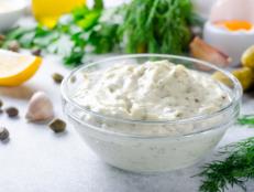 Homemade white sauce tartar tartare with ingredients pickles, capers, dill, parsley, garlic, lemon and mustard on a light stone background. Horizontal image