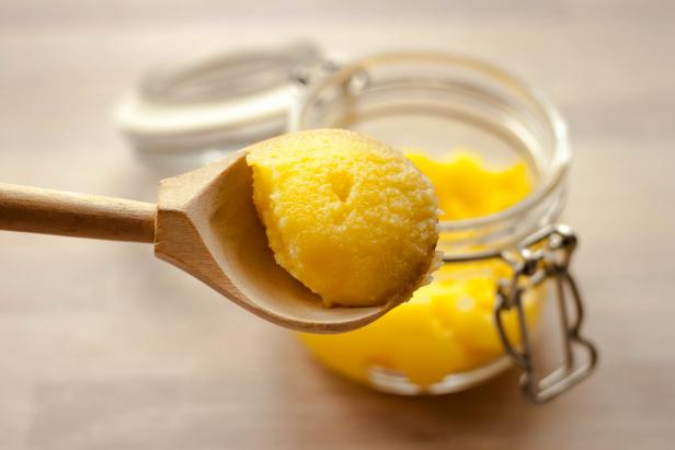 Ghee clarified butter desi yellow color in glass jar with spoon made from wood on natural wooden background close up view. Selective soft focus. Text copy space.