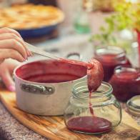 Young women preparing and canning fresh homemade strawberry jam, she pouring him into a jar