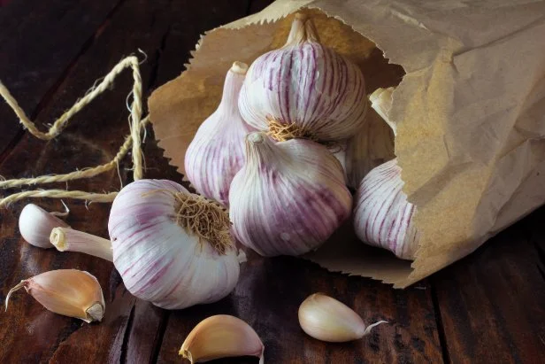 Garlic bulbs on packing paper, on rustic wooden table. Closeup of garlic bulbs.