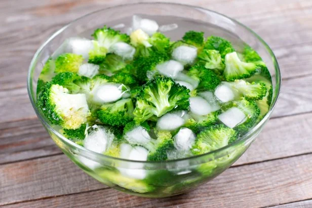 Blanched broccoli cabbage cooling down in icy water in a bowl on wooden table
