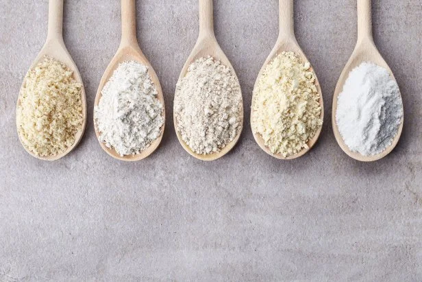 Wooden spoons of various gluten free flour (almond flour, amaranth seeds flour, buckwheat flour, rice flour, chick peas flour) from top view