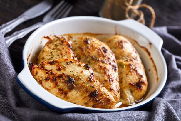 close-up of oven baked spicy juicy chicken breasts in a baking dish on a dark wooden table