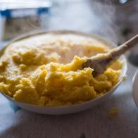 Close up of a wooden spoon serving polenta from a plate on a dining table.