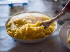 Close up of a wooden spoon serving polenta from a plate on a dining table.