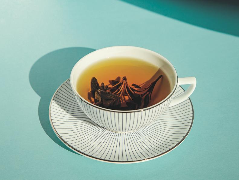 Herbal green tea in a white cup with a white saucer on color background