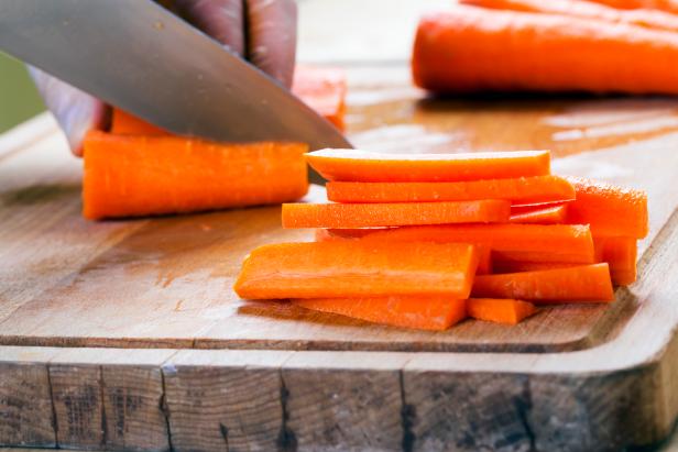 Man cutting carrot on table, closeup. Macro shot