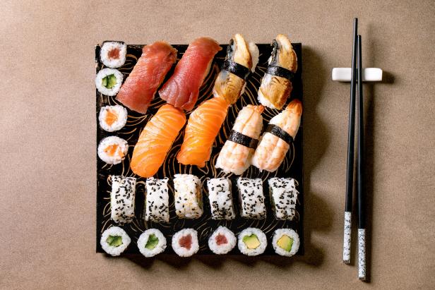 Sushi rolls set. Traditional japanese dish sushi and rolls with fresh salmon, tuna, eel and prawns on rice. Serving on black plate with chopsticks on brown background. Flat lay, copy space