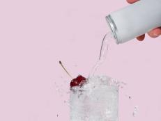 Sparkling water pouring from can into glass of ice with cherry.