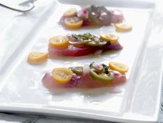 "Raw fish crudo with kumquats, marinated jalapeAos & fresh mint sitting on a white porcelain plate on a brightly lit table."