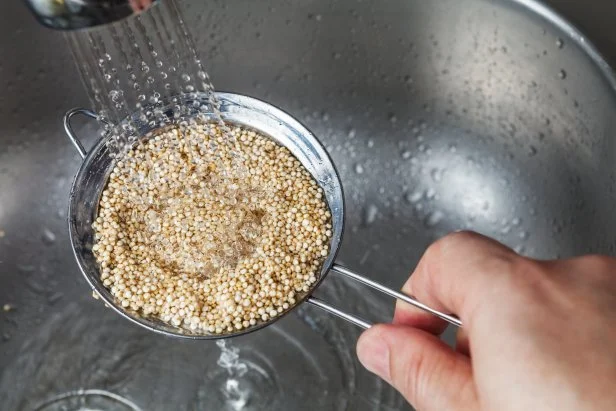 Man holding small strainer with raw quinoa seeds and rinsing it in cold water in the kitchen sink
