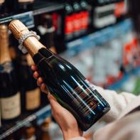 Close up shot of woman choosing a bottle of champagne from the shelf in a supermarket.
