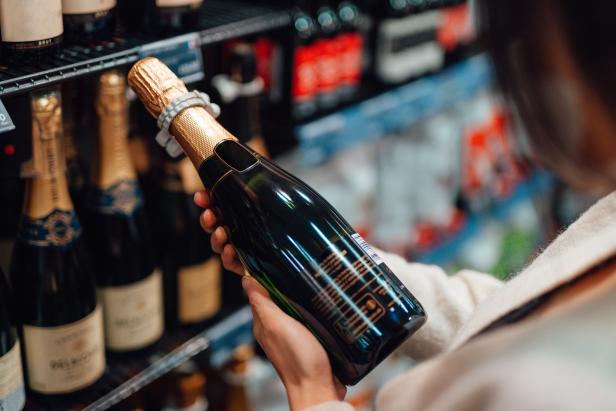 Close up shot of woman choosing a bottle of champagne from the shelf in a supermarket.
