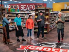 Host Guy Fieri and contestants Damaris Phillips, Justin Warner, and Maneet Chauhan look on while Beau Macmillan celebrates, as seen on Guy's Grocery Games, season 24.