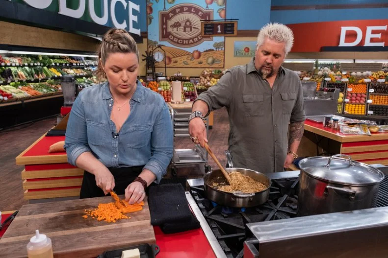 Host Guy Fieri helps contestant Damaris Phillips while she chops carrots, as seen on Guy's Grocery Games, season 24.