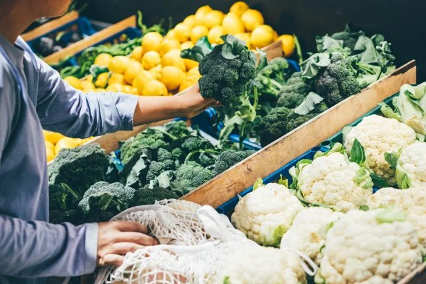 Woman choosing greenery and vegetables at farmer market and using reusable eco bag.