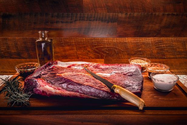 Raw brisket on a wooden cutting board with seasoning, salt and olive oil