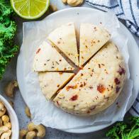 Vegan cashew cheese with dried tomatoes and spices on a white plate, gray background, top view. Alternative dairy-free diet, plant-based food.