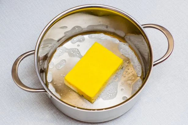 The yellow dishwashing sponge lies at the bottom of the soaped pan on the table.