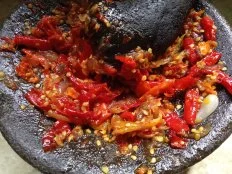The process of making chili sauce from red chili with a traditional handmade mortar. Indonesian cooking. homemade food. top view