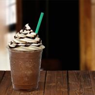 Frappuccino in takeaway cup on wooden table isolated on blackFrappuccino in takeaway cup on wooden table isolated on black