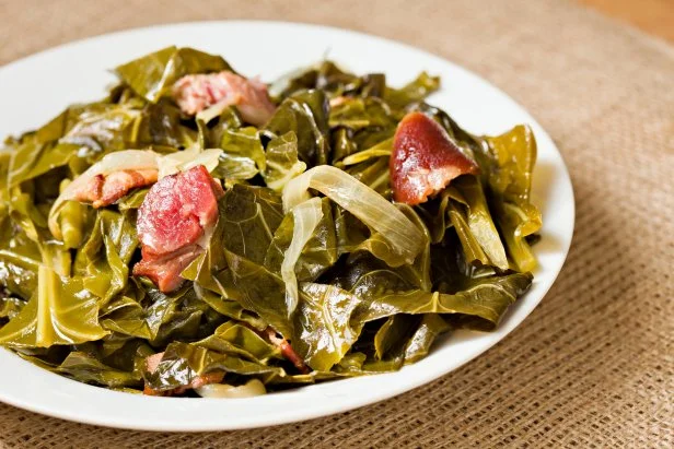 A high angle close up shot of a white bowl full of collard greens and ham hock pieces. 