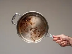 Dirty oily burnt metal frying pan held in hand by male hand. .