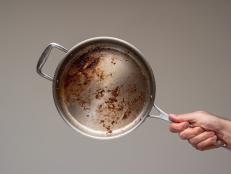 Dirty oily burnt metal frying pan held in hand by male hand. .