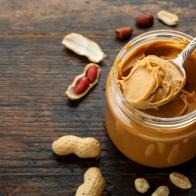 peanut paste in an open jar and peanuts in the peel scattered on the table