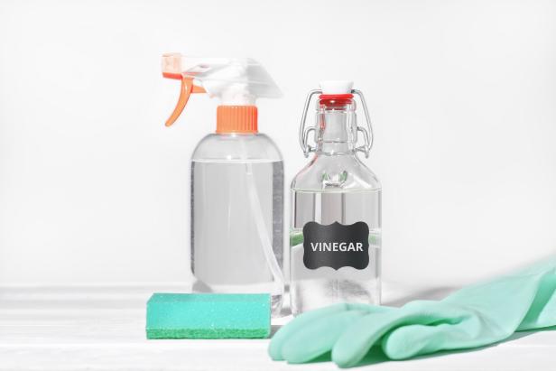 white vinegar for home cleaning chores, natural householding detergent, affordable product for housekeeping. rubber glove and kitchen sponge next to sprayer bottle
