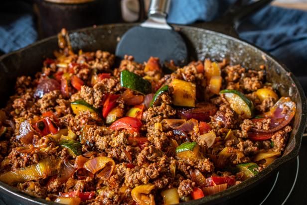 Delicious spicy and low carb pan dish with low fat ground beef and mediterranean vegetables served hot in a rustic cast iron pan on table background. Closeup view