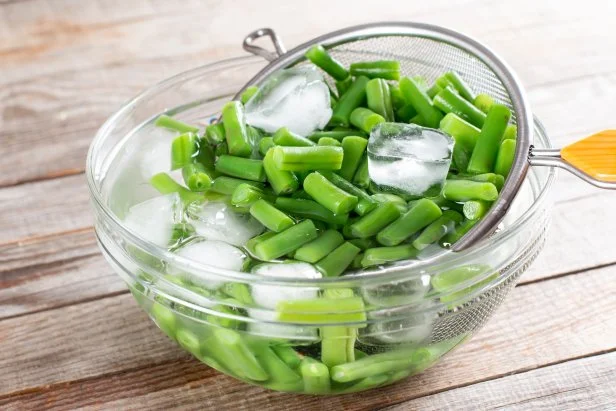 Green beans in a colander. Boiled or blanched vegetables on a wooden table