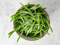 Frozen green beans, haricots verts,  close up in a bowl on light grey background, flat lay, copy space