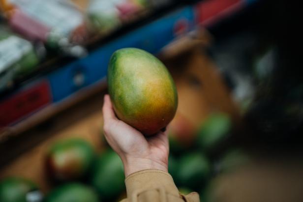 Cropped shot of female hand picking up a mango from the product aisle in the store.