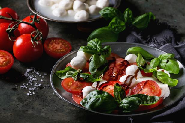 Italian caprese salad with sliced tomatoes, mozzarella cheese, basil, olive oil. Served in vintage metal plate with ingredients above over dark metal background. Close up. Rustic style. (Photo by: Natasha Breen/REDA&CO/Universal Images Group via Getty Images)