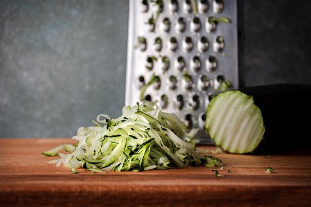 Frontal view of a pile of grated zucchini on a wooden cutting board with a grater, with gray background and copy space