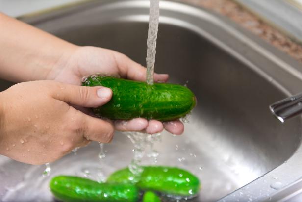 A closeup of male hands washing cucumber in the sink