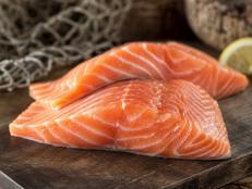 Fresh raw salmon fillets on a wooden board with lemon and fish net background.