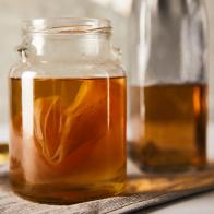 selective focus of jar with kombucha near bottle on grey napkin
