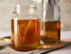 selective focus of jar with kombucha near bottle on grey napkin