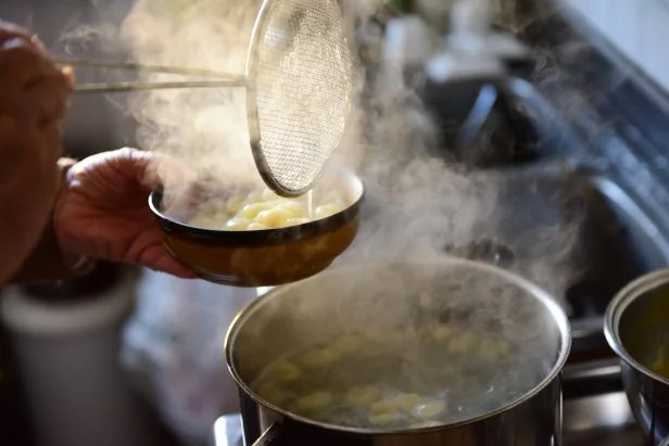 Straining home-made gnocchi out of a pot with boiling water using a steel colander into a bowl. One of the steps of the preparation of home-made gnocchi, Italian soft dough dumplings made with boiled potatoes and white flour.
