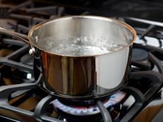 Water bubbles and boils on a gas stove or range in a home kitchen.  Blue flame and stainless steel pot.