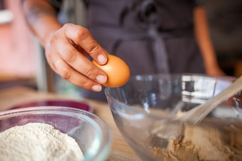 Cette photographie prÃ©sente une personne en train de cuisiner, casser un Å uf dans une prÃ©paration sucrÃ©e pour la rÃ©alisation d'un gÃ¢teau.