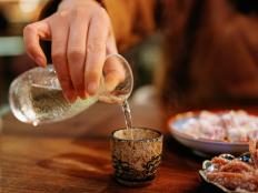 A close-up shot of a hand pouring sake in a tavern